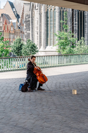 Ghent, Belgium - July 31, 2016: Musician playing cello under the Stadshal in Ghent. The construction...