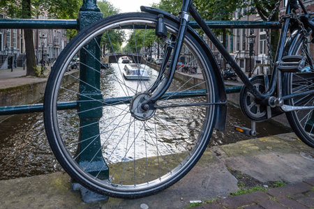 Amsterdam, Netherlands - August 09, 2016. Canal view in Amsterdam, view through bicycle wheel parked on bridge. Day in summerのeditorial素材