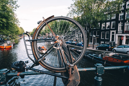 Amsterdam, Netherlands - August 09, 2016. Canal view in Amsterdam, view through bicycle wheel parked on bridge. Day in summerのeditorial素材