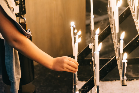 A young woman lighting the candles in a church. Horizontal compositionの写真素材