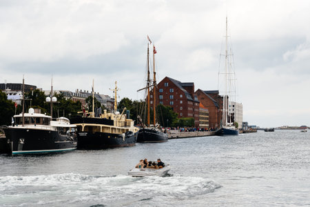 Copenhagen, Denmark - August 12, 2016: Boat with tourists on Copenhagen's harbor surrounded by  moored boats. Happy people in a cloudy summer day.のeditorial素材