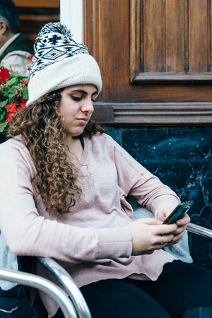 Teenage girl in knit hat texting with cell phoneの写真素材