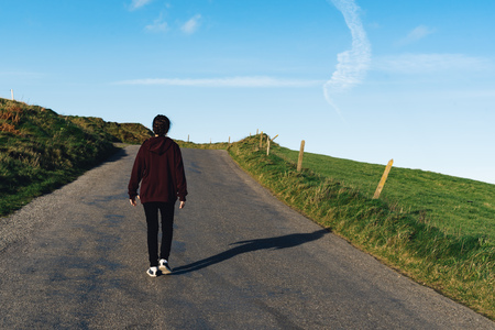 Young woman walking on lonely road next to green fields