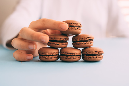 Woman placing macarons on heap on blue tableの写真素材