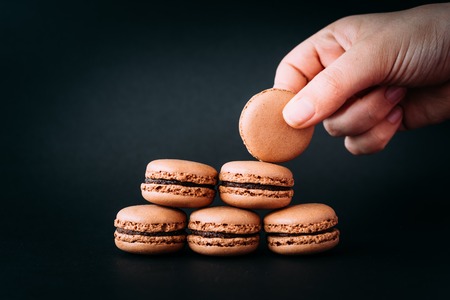 Woman placing macaroons on heap on black backgroundの写真素材