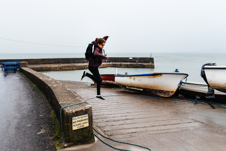Woman wearing casual clothes jumping at harbor in Irish coastの写真素材