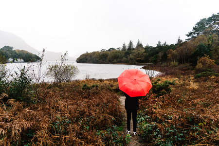 Woman with red umbrella by lake in Ireland