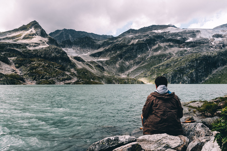 Adult man sitting at mountain lake in the Alpsの写真素材