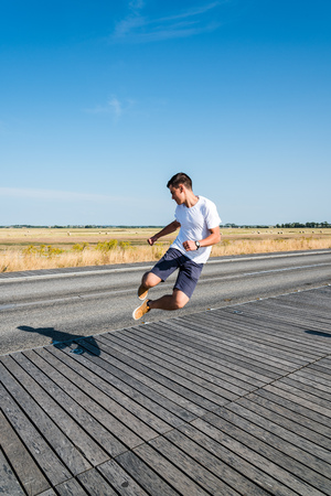 Young man jumping on boardwalk against landscapeの写真素材