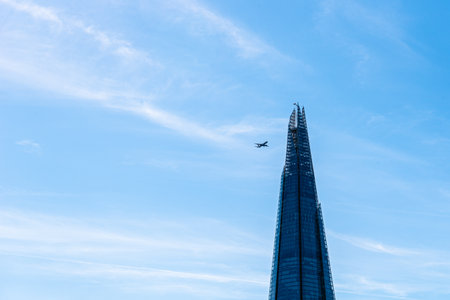 Plane flying over skyscraper against blue skyのeditorial素材