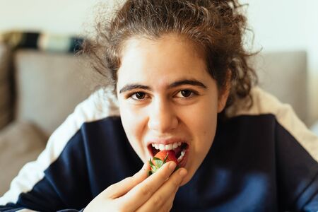 Happy girl eating strawberry at home
