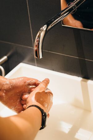 Close-up of young man washing hands with soap under bathroom sink.の写真素材