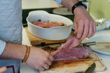 Midsection of man cutting roast meat on table at kitchenの写真素材