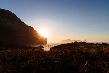 Scenic view of rocky promontory in the coast at sunset with the sun flare