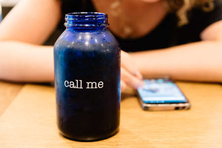 Glass with the Text Call Me on Background of Woman texting on Phone Waiting for answer or Phone Callの写真素材