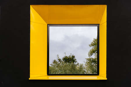 Yellow window on black facade with reflection of green tree on.の写真素材