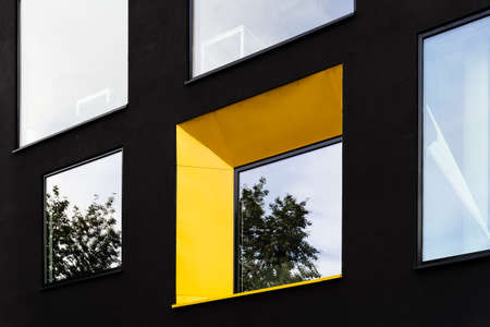 Yellow window on black facade with reflection of green tree on.の写真素材