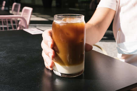Woman hand holding tasty glass of cold brew coffee with milkの写真素材