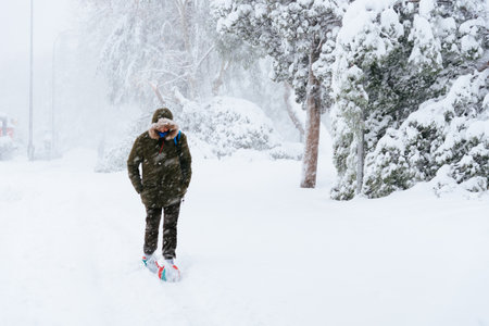 Man walking on a city street covered in snow during heavy snowfall with fallen treesのeditorial素材