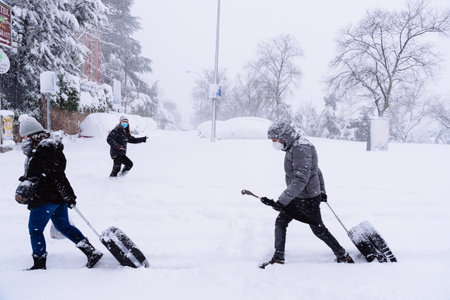 People carrying trolleys on a city street covered in snow during heavy snowfall storm in Madridのeditorial素材