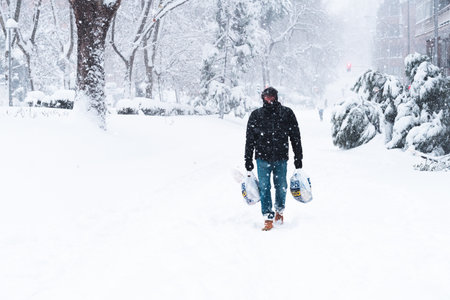 Man walking on a city street covered in snow during heavy snowfall storm with fallen treesのeditorial素材