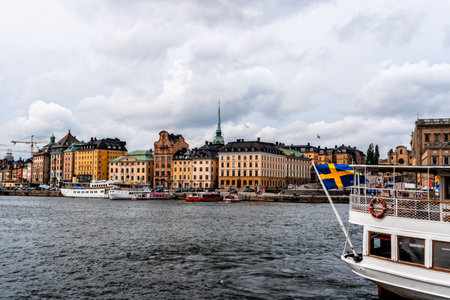 Tour boat with swedish flag navigating against waterfront of Stockholmのeditorial素材