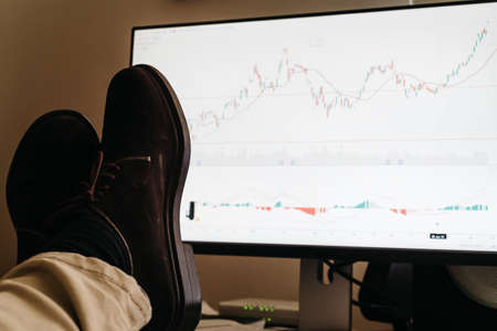 View of the broker feet on the trading desk in front of the stock market charting screen