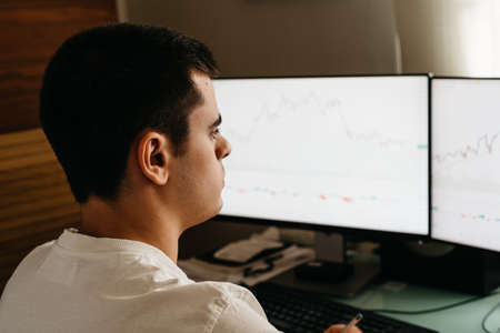 Successful young trader in casual wear working with charts and market reports at home