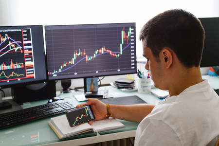 Successful young trader in casual wear working with charts and market reports at homeの写真素材