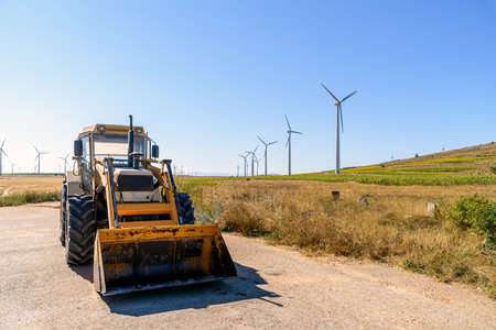 Excavator against wind turbines generating electricity on landscape of farmland