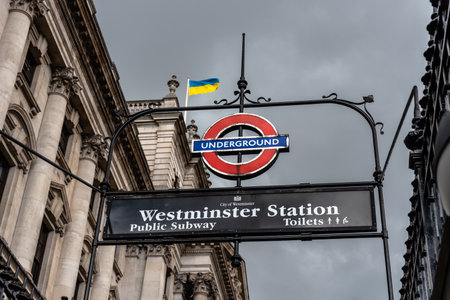 London, UK - August 26, 2023: Close-up view of the London Underground sign in Westminster Station against cloudy sky and Ukrainian flagのeditorial素材