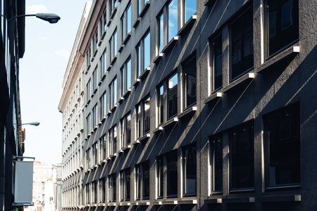Sunlight casts shadows on a dark building's facade, highlighting the many windows along a city street.の写真素材