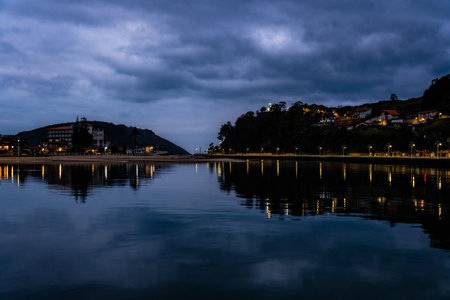 Night view of a calm bay reflecting the lights of buildings on the hillsides and the cloudy sky. Ribadesellaの写真素材