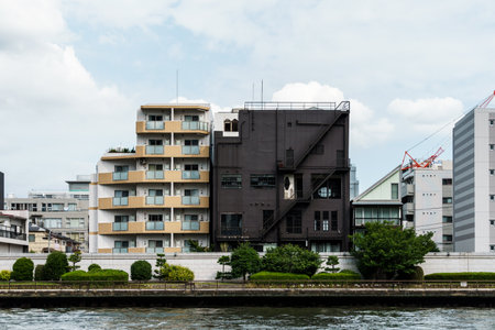 Residential buildings line the riverbank under a cloudy sky, showing diverse architectural styles in...