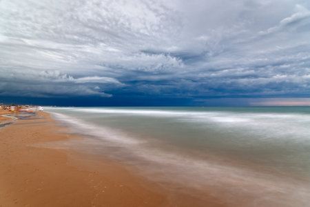 A long exposure captures the motion of the waves as they meet the shore under a dramatic, cloudy sky at the beach. Cut-off lowの写真素材