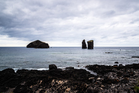 Two rocky islets stand tall in the Atlantic Ocean under a cloudy sky, creating a dramatic seascape...