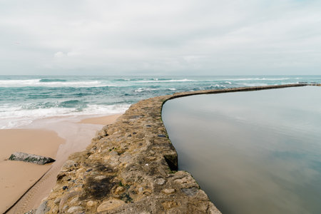 Azenhas do Mar showcases its unique charm with a natural pool meeting the ocean under a soft, overcast sky in Portugal.の写真素材