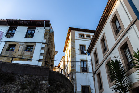 Sunlight illuminates the walls of two buildings, one whitewashed, the other stone, in a narrow street. Lastres, Asturiasの写真素材