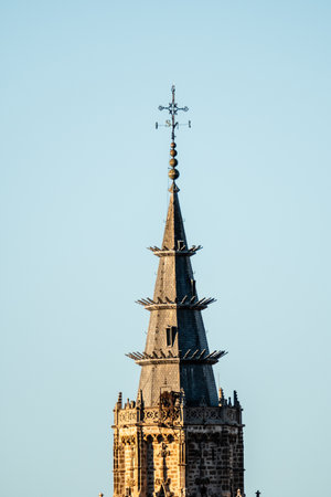 The detailed spire of Toledo Cathedral against a clear sky displays intricate stonework and a...