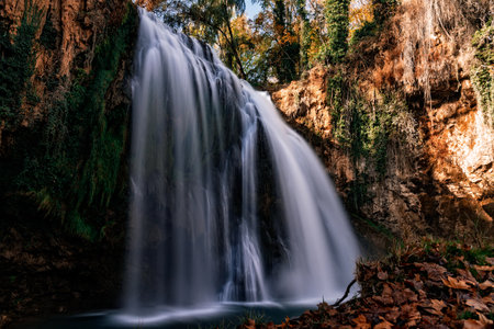 Smooth flowing waterfall creating a tranquil scene in an autumn forest, surrounded by moss, rock cliffs, and colorful leaves in Monasterio de Piedra, Spainの写真素材