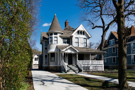 Chicago, USA - April 14, 2025: Victorian house standing on a corner lot featuring a white picket fence and dormant trees