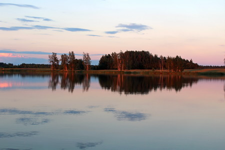 Magnificent summer nature on a pond in July. Trees, field and pond in the rays of the setting sun.の写真素材