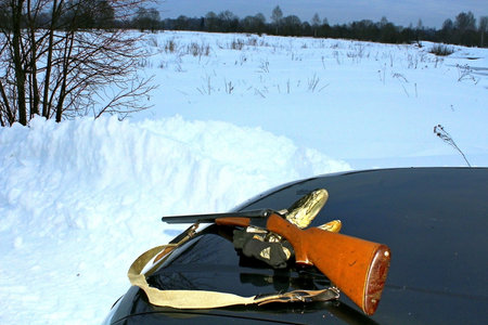Old hunting rifle on the hood of a car in the winter forestの写真素材