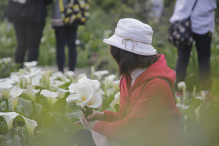 A young woman in a red jacket and white hat standing in a flower garden.の写真素材