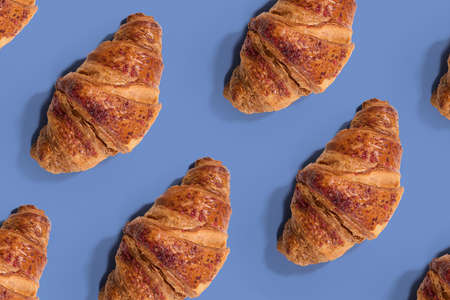 Fresh creme croissants on blue background. Bakery pattern croissants sprinkled with pink grains