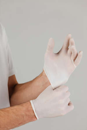 Man in white clothes and protective respirator wears white medical gloves on his hands. Studio photo on grey background.の写真素材