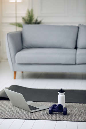 Equipment for training at home. Cropped photo of dumbells, laptop and bottle of water.