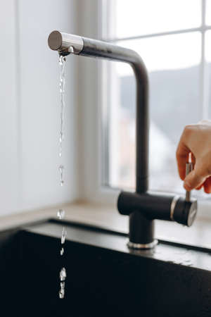 Woan is opening and closing water flow tap and filling sink with water. Water running from chrome faucet. Bathroom plumbing. Using water resources.の写真素材