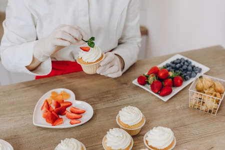 Female baker decorating cupcakes with colored berries.の写真素材