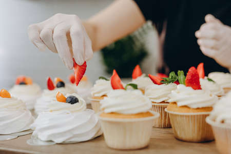 Close shot of many sweet cupcakes on the foreground while a baker decorating the last one.の写真素材